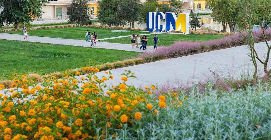 Image depicts a scene of grass, sidewalks and a large UCM at UC Merced.