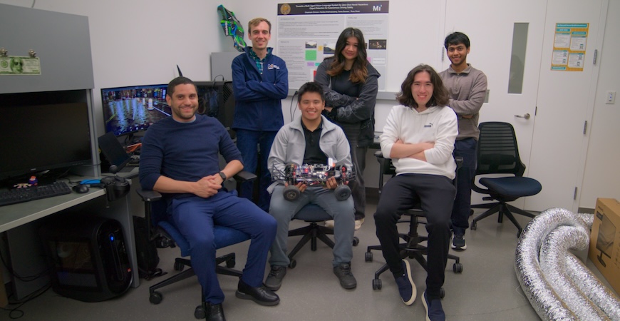 Students and Professor Ross Greer are pictured in his lab, holding a small car with a processor affixed to the top of it.